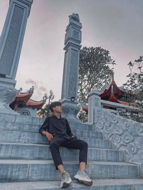 17 Khoảnh khắc chàng trai k8 ngồi trên bậc đá ở khu đền, phía sau là cột cao và mái cong cổ kính, tư thế ngả người thoải mái khiến ảnh vừa trẻ trung vừa có chiều sâu, hợp đăng Instagram kiểu du lịch nhẹ