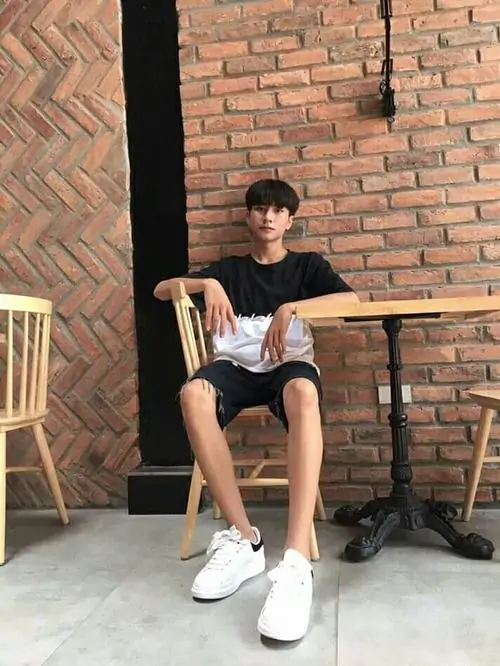 18 Nam sinh 2k8 ngồi trên ghế trước nền gạch mộc, áo tối và quần short khiến tổng thể giản dị nhưng không nhạt, cách đặt chân thoải mái cùng ánh sáng tự nhiên làm bật khí chất học đường và vẻ gần gũi