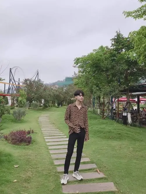 19 Góc ảnh hot boy 2k8 đặt nhân vật ở xa trên lối đi giữa vườn xanh, áo nâu và quần tối hòa cùng khung cảnh yên, bức ảnh thiên về cảm giác đời thường, hợp nhóm ảnh nam sinh sân trường hoặc công viên