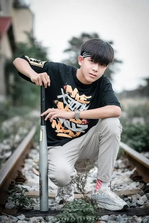 21 Ảnh trai đẹp k8 bắt khoảnh khắc nam sinh ngồi thấp trên mặt sân, lưng dựa hàng rào và mắt hướng xa, sắc xám bao phủ khung hình làm áo sáng nổi hơn, tạo cảm giác trong veo đúng chất thanh xuân học đường