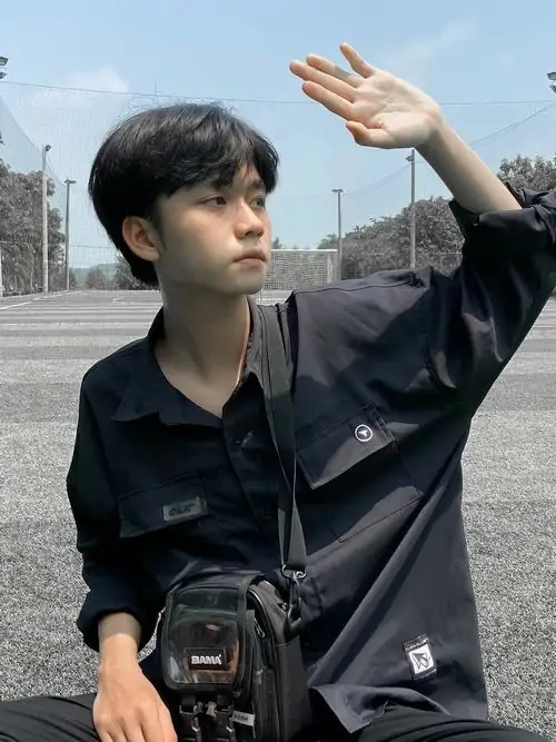 24 Giữa khoảng đất trống và bóng cây cao, chàng trai 2008 ngồi co gối trong áo đen, tư thế trầm và ít biểu cảm tạo chiều sâu, bức ảnh nghiêng về cảm giác thanh xuân lặng hơn là kiểu phô diễn thần thái