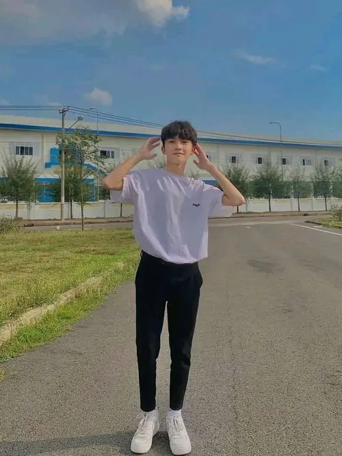 29 Khung hình nam sinh điển trai với áo khoác tối màu và cử chỉ vuốt tóc giữa không gian đầy nắng, gương mặt nghiêng nhẹ làm jawline rõ hơn, bức ảnh thiên về sự sáng sủa và cảm giác gần gũi kiểu đời thường