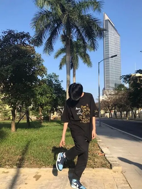 6 Một bạn trai 2008 bước trên lối đi rợp nắng có hàng cọ phía sau, đồ tối màu khiến thân hình nổi rõ giữa nền xanh, ảnh gợi chất boy phố nhẹ nhưng vẫn giữ vẻ trong trẻo rất đúng tinh thần học sinh cuối cấp