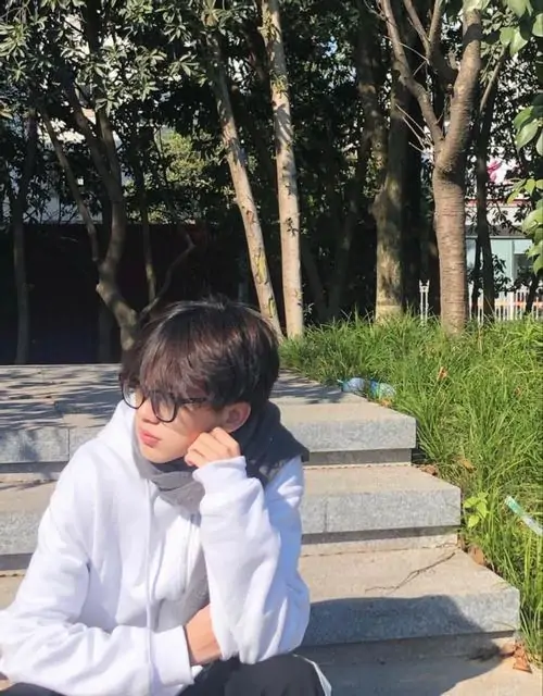 5 Cậu trai k9 đeo kính ngồi nghỉ trên bậc thang với hoodie trắng tay chống cằm để lộ sống mũi cao và kiểu tóc layer tỉa mỏng của nam sinh lớp 11.