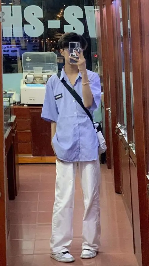 8 Chàng trai mặc đồng phục sơ mi xanh quần trắng đứng trong hành lang với túi đeo vai toát lên gu thời trang sơ mi trắng cà vạt của nam sinh cấp ba.