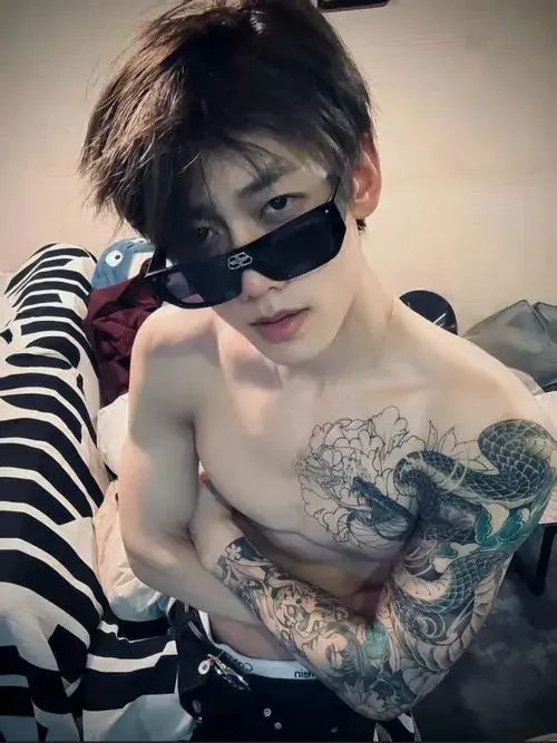 10 Cậu trai đeo kính râm nằm nghiêng trên giường, thân trên để trần khoe mảng xăm lớn ở vai ngực, bức ảnh có độ nóng bỏng vừa phải, hợp phong cách chàng trai phong trần thích phô diễn cá tính theo cách khá tự nhiên