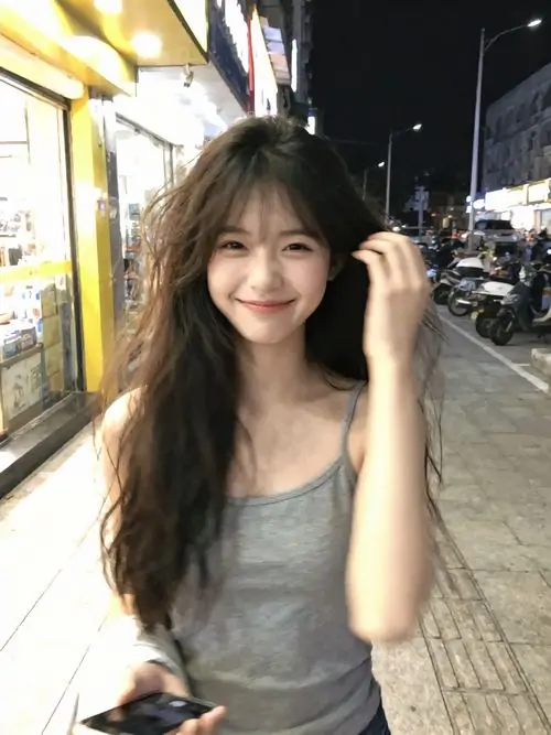 36 Trên phố tối, cô gái mặc áo sát nách xám cười rạng rỡ khi một tay chạm tóc, ảnh gái đẹp mang nhịp trẻ trung nhờ ánh đèn đường và phong cách dạo phố nữ tính tạo cảm giác vừa vui vừa ngầu