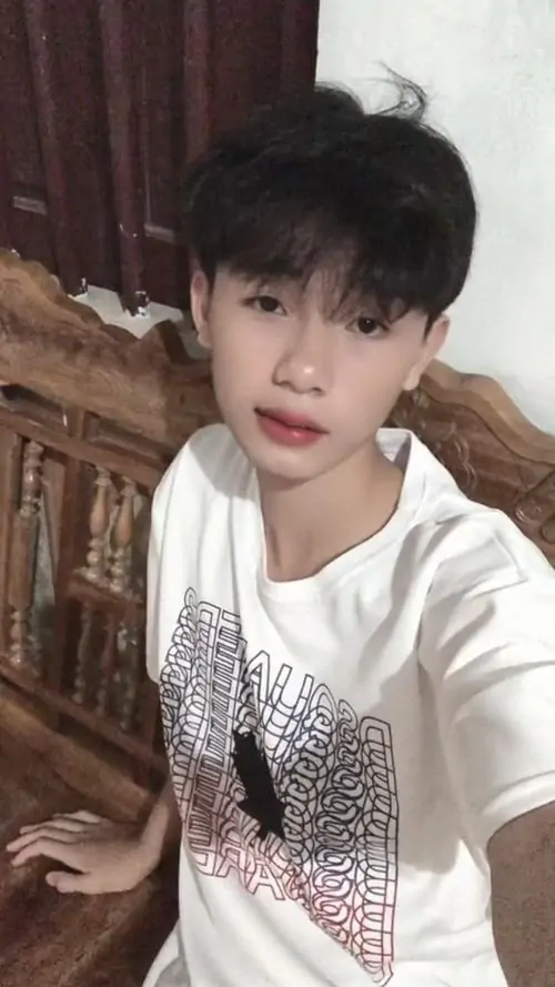 13 Hình ảnh chàng trai với kiểu tóc hiện đại tôn gương mặt và nụ cười tự tin trong áo thun trắng lấp lánh đang ngồi trong phòng. Cậu chàng khoe dáng vẻ khỏe khoắn và vibe học đường hiện đại của hotboy 2k11.