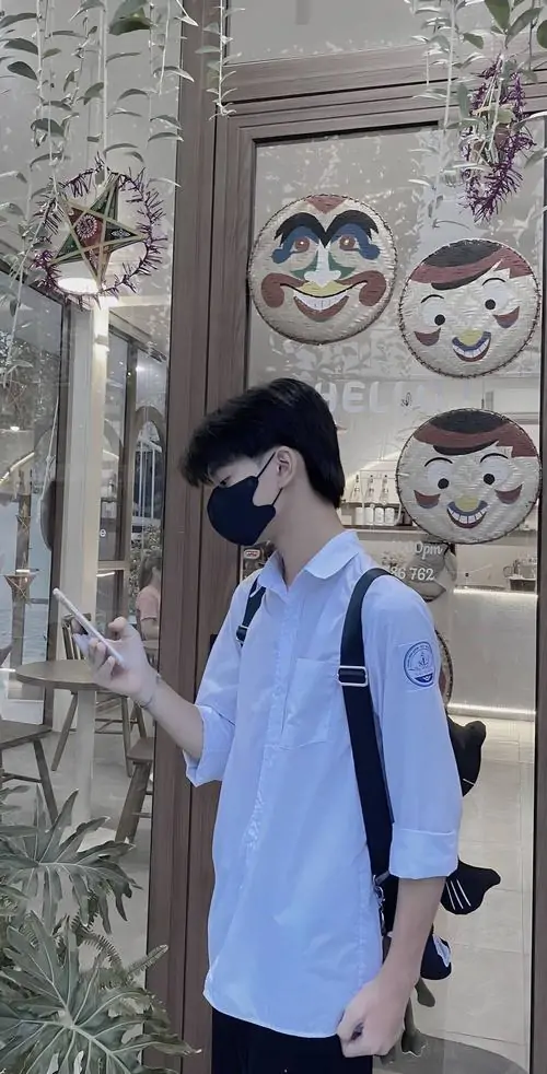 2 Cậu bạn cấp 2 mặc áo sơ mi xanh quay nhẹ sang bên, tay giữ điện thoại ngang mặt để giấu đi biểu cảm, góc nghiêng tạo cảm giác cool ngầu, phù hợp làm avatar nam sinh giấu mặt trên mạng xã hội