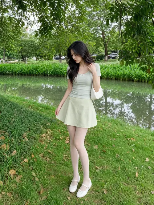 8 Trong trung tâm thương mại, người mẫu diện đầm ngắn xanh, xách túi da và đứng cạnh lan can sáng.