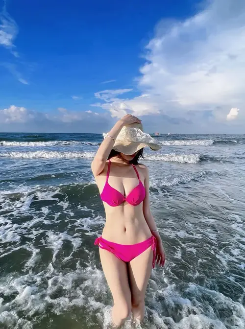 23 Cô gái mặc bikini xanh ngồi bên mép nước, ôm đầu gối và quay mặt về phía sóng nhỏ.