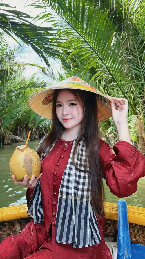 1 Cô gái đội nón cói mặc áo đỏ, cười nhẹ giữa hàng dừa xanh mát